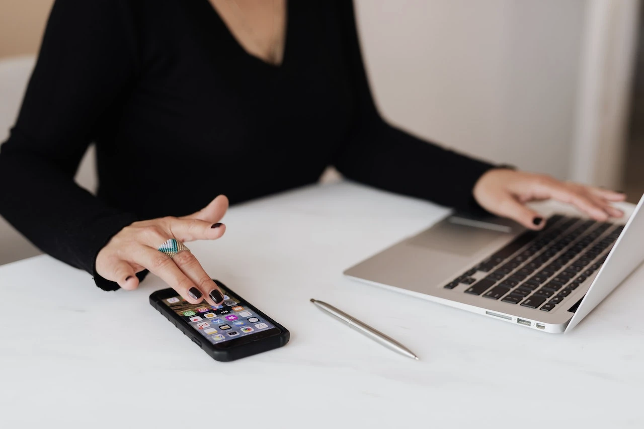 an image of a person working at a laptop while also working on a phone